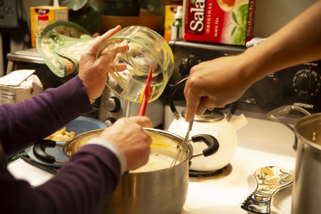 Two people's hands, adding ingredients and stirring a pot