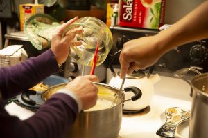 Two people's hands, adding ingredients and stirring a pot