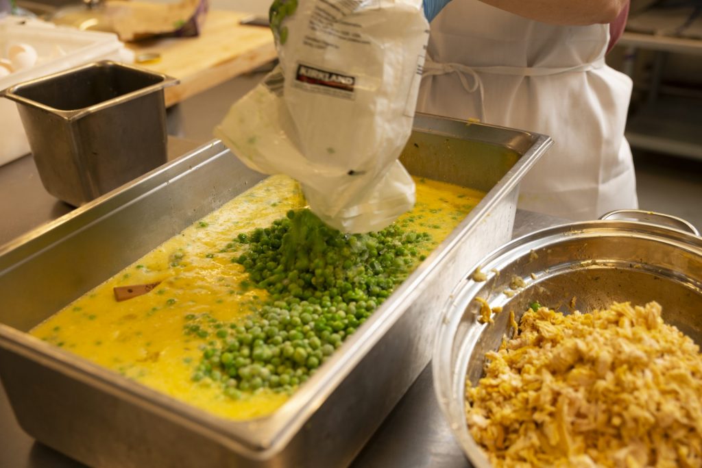 A large container of egg mixture with frozen peas being poured in