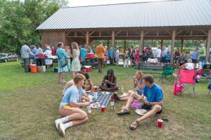 People sitting on the grass eating in the foreground with more people and a pavilion in the background