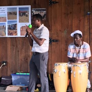 A speaker with microphone and a man with drums in the background