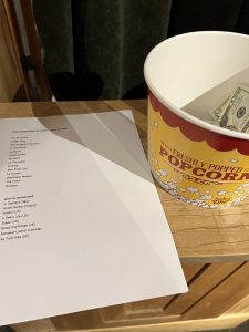 Movie list next to a popcorn container serving as a donation receptacle. Image: K. McCracken.