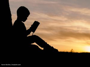 Silhouette of a boy reading against the evening sky. Image: Aaron Burden, Unsplash.com